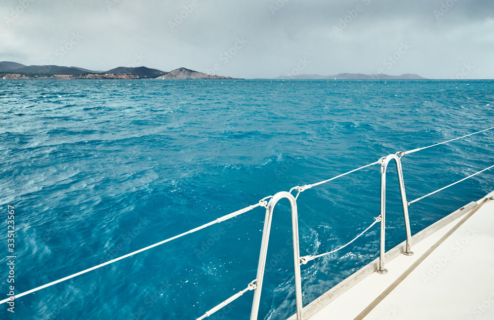 The view of the sea and mountains from the sailboat, edge of a board of the boat, slings and ropes, splashes from under the boat, rainy weather, dramatic sky