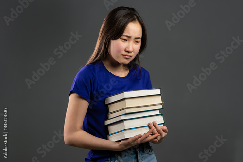 Asian student is dissatisfied wit homework books.Girl with books, she is annoyed