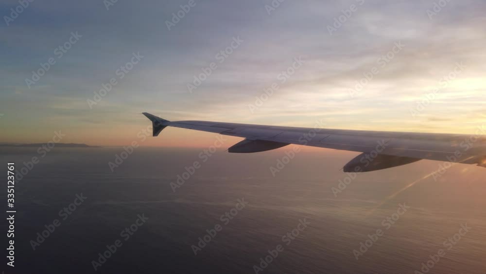 Wing side view of a plane flying over the Pacific Ocean at sunset
