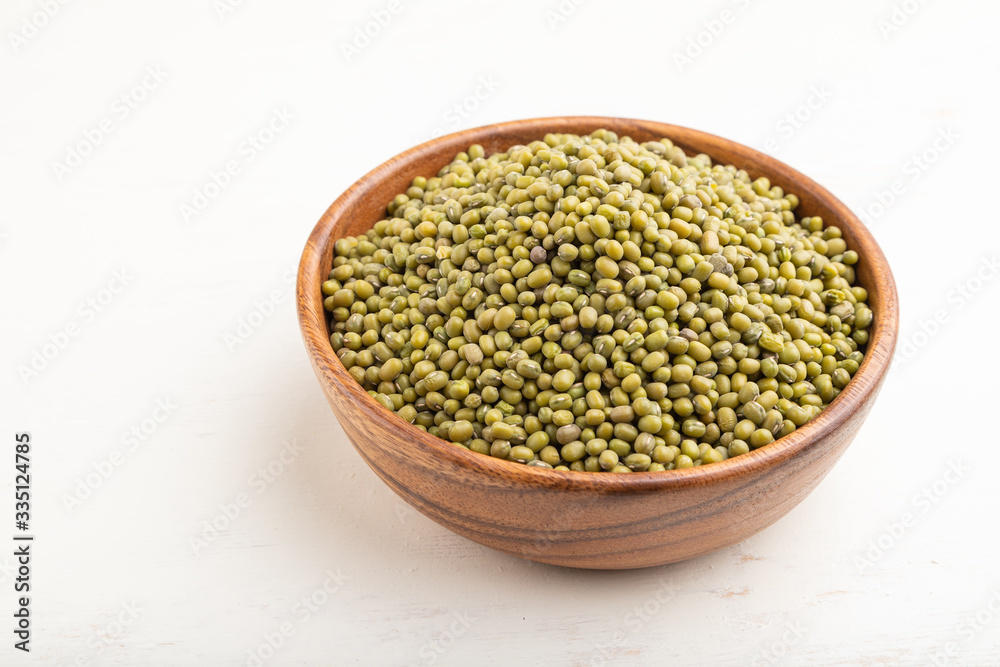 Wooden bowl with raw green mung bean on a white wooden background. Side view. Wooden bowl with raw green mung bean on a white wooden background. Side view.