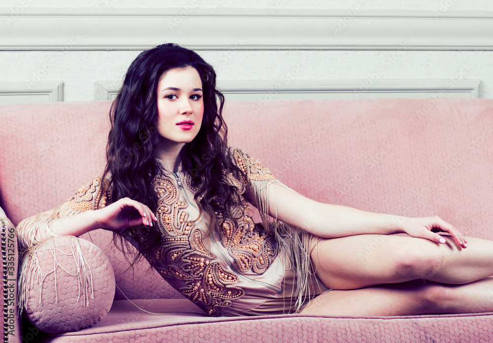 Naklejka premium young pretty brunette girl in fashion dress on sofa posing in luxury rich home interior, lifestyle modern people concept