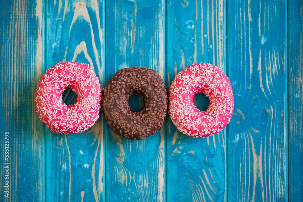Three different doughnuts lie on a blue wooden background.