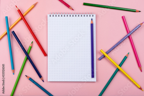 notebook on a pink background. Colored pencils are scattered nearby.