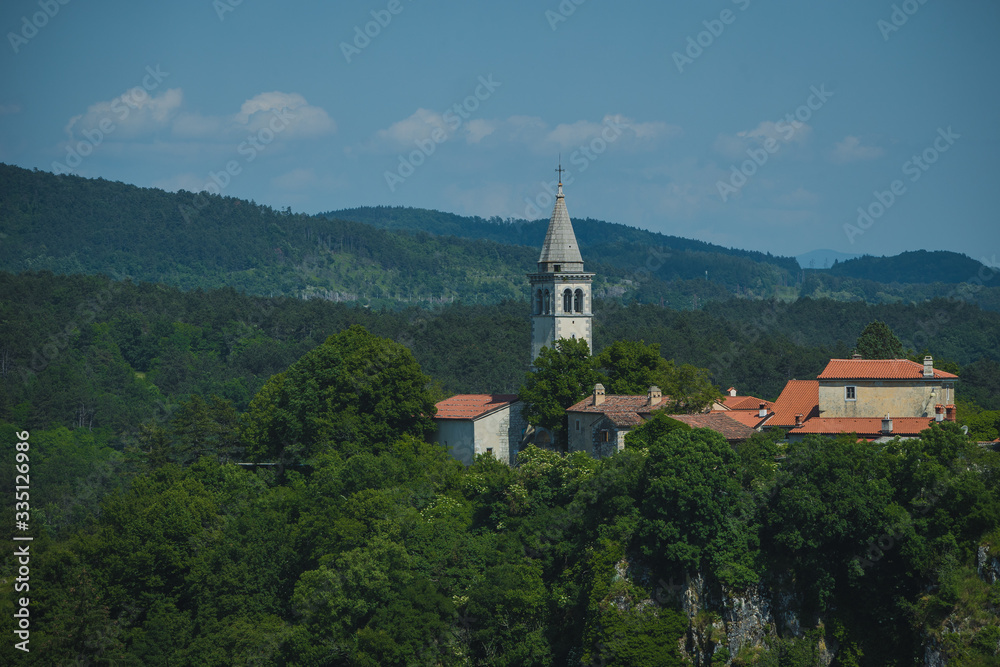 Village of Skocjan, with a visible bell tower of St. Kancijan church, rising way above the Skocjan Caves gorge on a summer day.