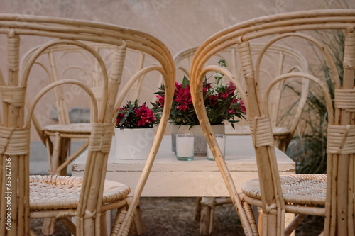 Decoracion de sala de estar con sillas de mimbre  mubles de madera  velas  flores rojas y almohadones blancos.