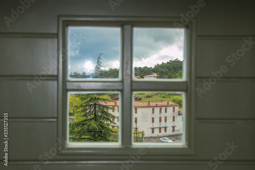 Panorama of the city of Stanjel in Slovenia on a cloudy spring day, looking through window with a wooden cross on it.