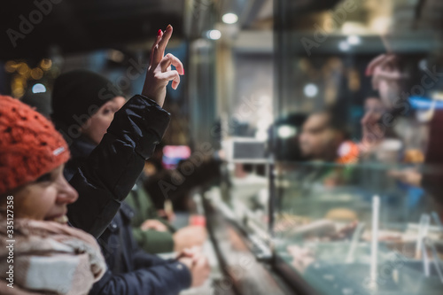 Person ordering a fresh kebab or gyros in a fast food stall or vendor outside in a city. Visible hands showing V sign to order food over the counter in festive evening. © Anze