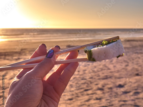 Woman holding sushi at sunset on the beach