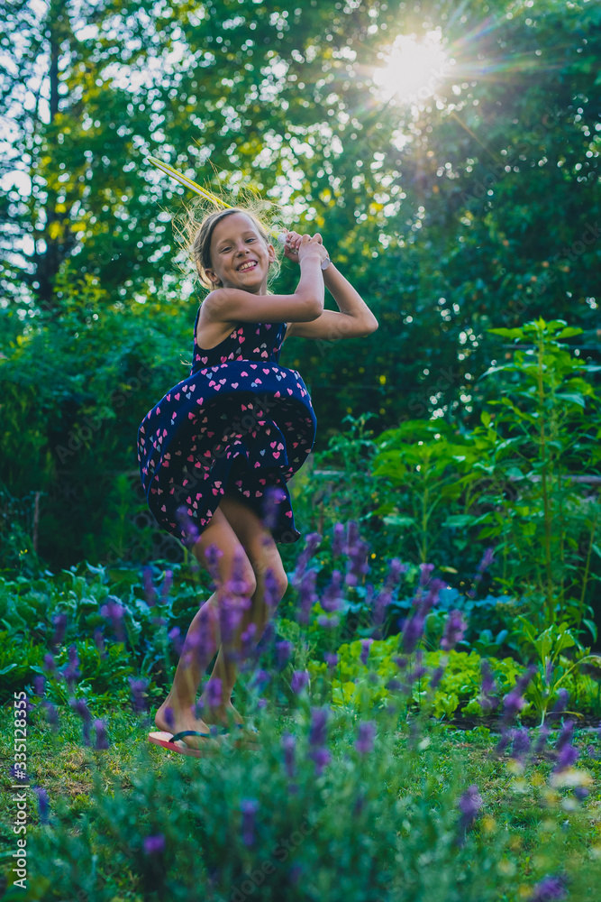Young caucasian girl or kid is playing badminton game in a lush green garden. Kid jumping high up into sun while playing badminton Young caucasian girl or kid is playing badminton game in a lush green garden. Kid jumping high up into sun while playing badminton