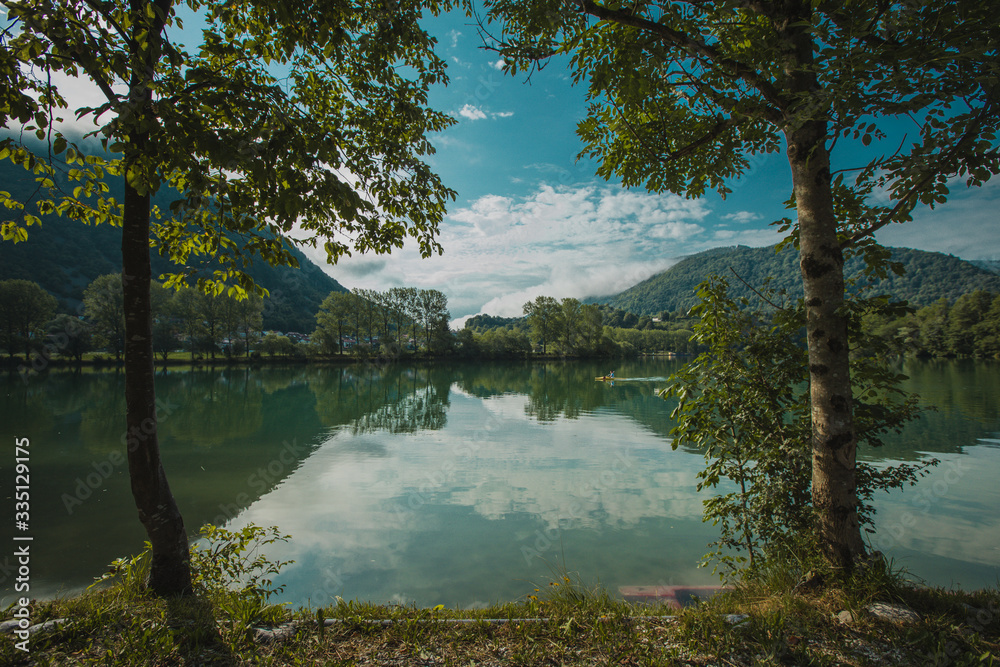 Tranquil lake of Soca river at Most na Soci in early morning. View from between the trees towards a gravel path next to the lake.
