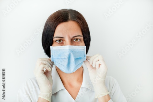 Tired experienced female doctor in uniform, gloves adjusts protective mask. Protection from Covid-19 coronavirus.