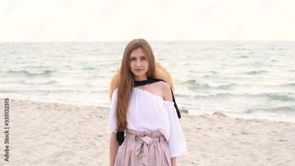 Beautiful girl with long brunette hair in straw hat, shirt and skirt is walks along sea Beautiful girl with long brunette hair in straw hat, shirt and skirt is walks along sea
