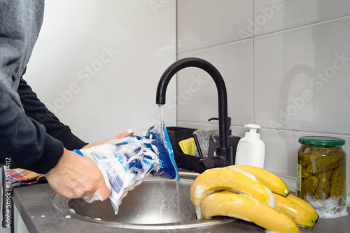 Side view on hands of unknown caucasian man person holding a rice bag under sink tap washing food with soap cleaning disinfection in water to disinfect from viruses or pollution at home in kitchen