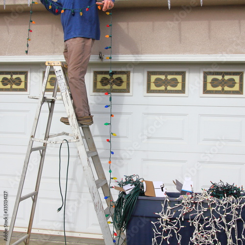 Man stringing Christmas lights on his house.
