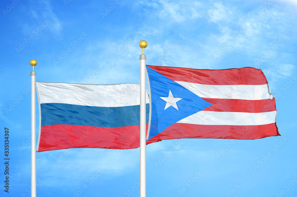 Russia and Puerto Rico two flags on flagpoles and blue cloudy sky