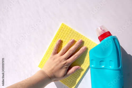 House cleaning and disinfection, prevention of coronavirus. A blue bottle of chlorine-free disinfectant and a woman's hand wiping the white surface with a cellulose cleaning cloth close-up with copy s