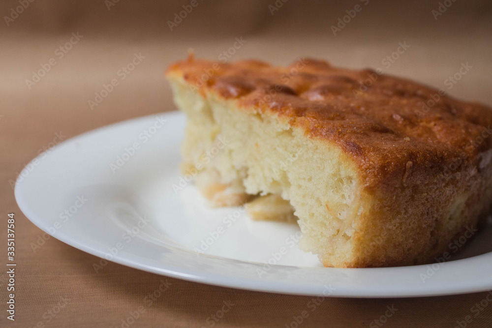 Sweet homemade cakes with apples. A slice of sponge Apple pie with a ruddy crust on a white plate close-up on a beige textile linen background.