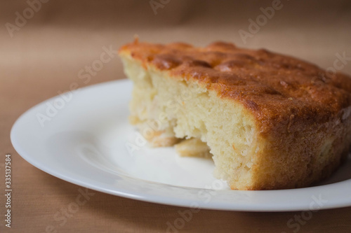Sweet homemade cakes with apples. A slice of sponge Apple pie with a ruddy crust on a white plate close-up on a beige textile linen background.