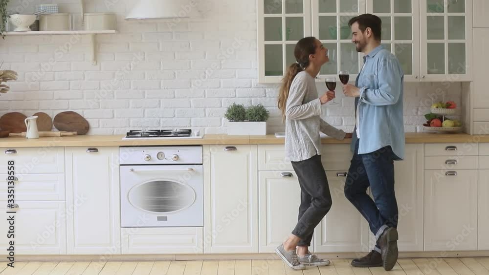 Full length happy mixed race woman chatting with handsome young man in modern kitchen. Positive family couple holding glasses of wine, enjoying pleasant conversation together at home dating. Full length happy mixed race woman chatting with handsome young man in modern kitchen. Positive family couple holding glasses of wine, enjoying pleasant conversation together at home dating.