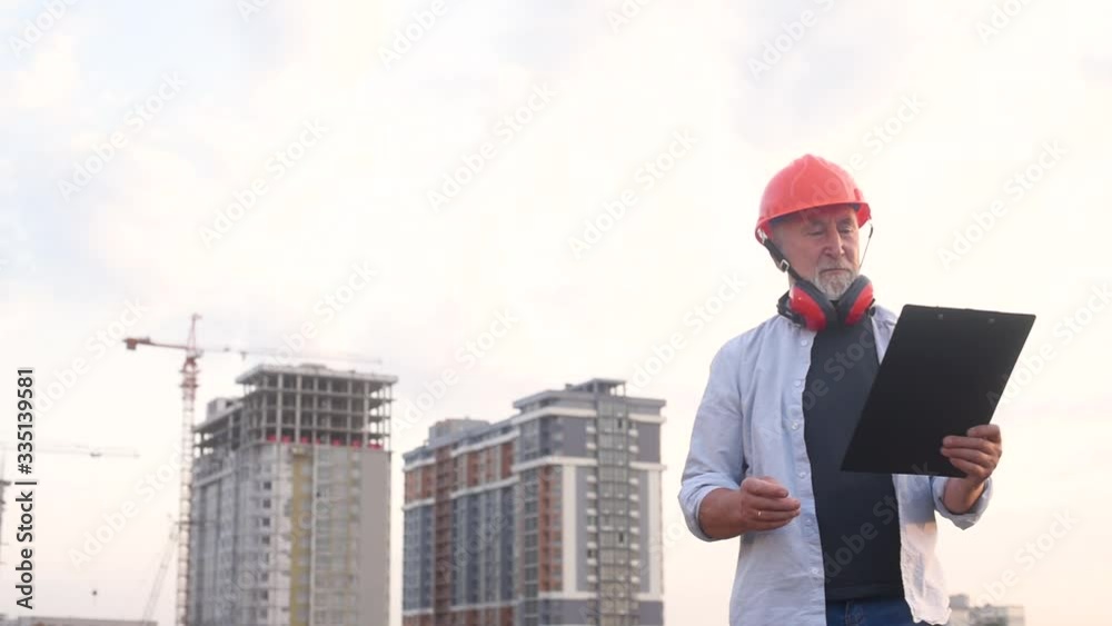 Senior man builder engineer in helmet with a gray beard on the background of construction Senior man builder engineer in helmet with a gray beard on the background of construction