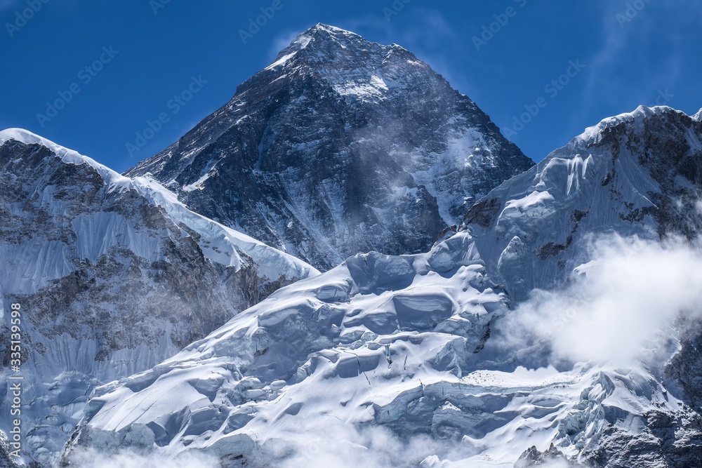 Mount Everest on center background with mountains both sides in front and few clouds 