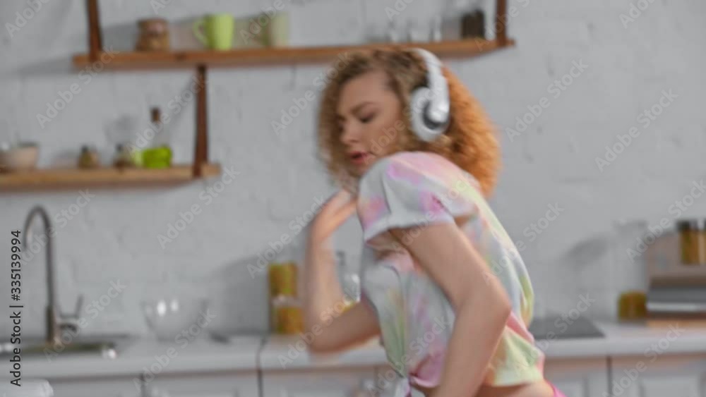 Girl in headphones with smartphone dancing near apples and cereals in kitchen Girl in headphones with smartphone dancing near apples and cereals in kitchen
