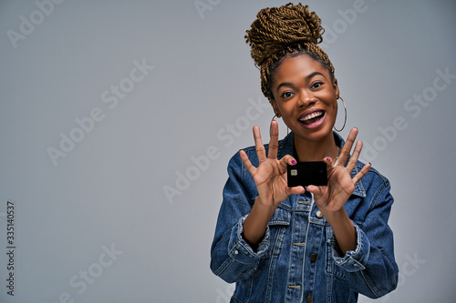 A girl with a smile in a jeans jacket shows a black bank credit card in her hands. Banking concept