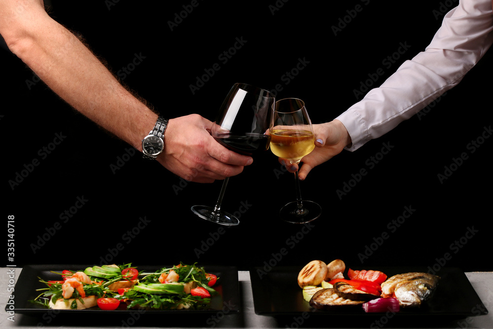 couple clink glasses on dark background and food on table. dinner concept with man and woman couple clink glasses on dark background and food on table. dinner concept with man and woman