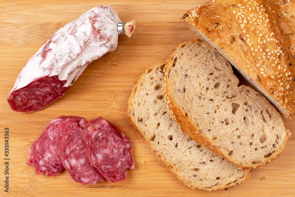 Baked sausage and several sliced sausage slices next to sliced whole grain bread on a wooden board. The concept of simple affordable food. Baked sausage and several sliced sausage slices next to sliced whole grain bread on a wooden board. The concept of simple affordable food.