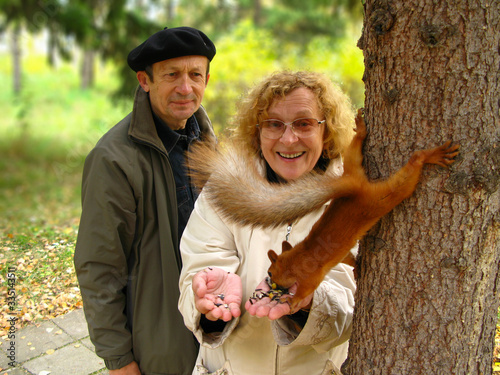 Happy smiling senior citizens feed a squirrel in the park. The concept of ecology, strengthening family relationships and hiking.