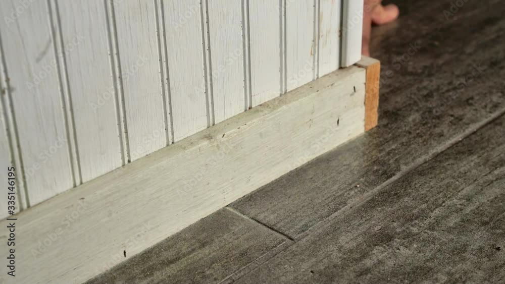 Mans hand sanding down a white baseboard and kitchen island in