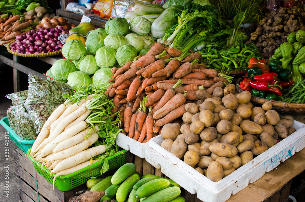 A display of vegetables in the market with radish, carrots, potatoes, cabbages, red bell peppers, ginger, and leafy vegetables