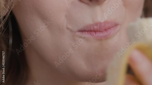 Detail shot of caucasian woman mouth eating chews banana liten natural window light