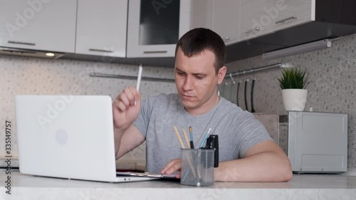 A young man has difficulty working remotely from home and holds his hands behind his head while sitting at a table