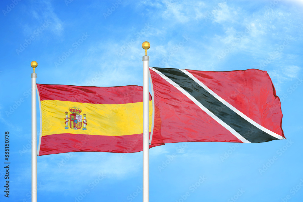 Spain and Trinidad and Tobago two flags on flagpoles and blue cloudy sky Spain and Trinidad and Tobago two flags on flagpoles and blue cloudy sky