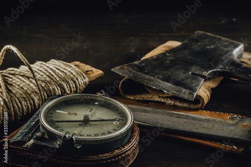 Old military compass, rusty hunting bushcraft knife, small axe and a linen rope on the dark wooden table. Leather cases, front view, survival hunting concept. photo