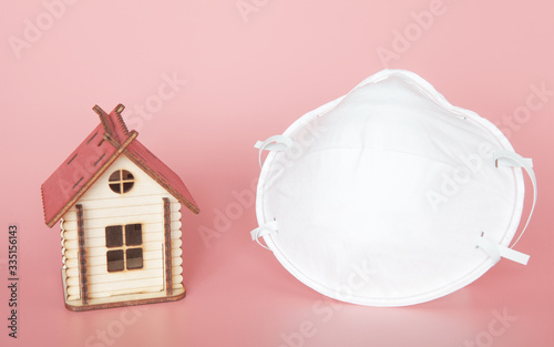 Medical mask with wooden toy house on a pink background. The concept of the fight against coronavirus and the request to stay at home