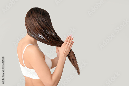 Beautiful young woman applying coconut oil on her hair against grey background