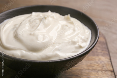 Bowl of tasty sour cream on wooden table, closeup