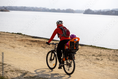 Woman with baby on bike rides on sandy shore near water