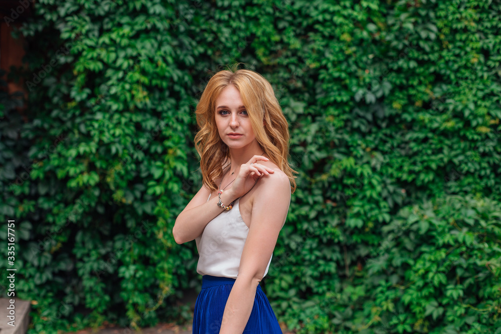 Portrait of a young beautiful woman, standing next to the wall of wild grape leaves holding a strap of a blouse. Portrait of a young beautiful woman, standing next to the wall of wild grape leaves holding a strap of a blouse.