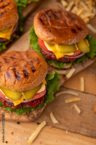 Juicy grilled burger on a wood table. Cheeseburger on the cutting board with beef, cheese, onions, tomatoes, cucumbers and french fries. Fast food. Top view. Rustic style