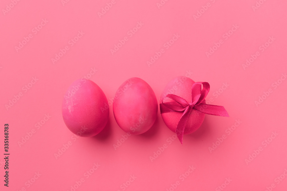 Bright pink eggs with satin bow on a pink background. Festive spring concept. Color trend.