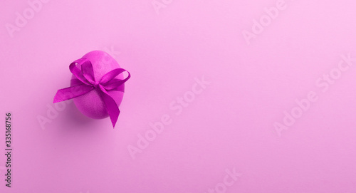 Bright pink egg with a satin bow on a pink background. Festive spring concept. Color trend. Selective focus close-up.