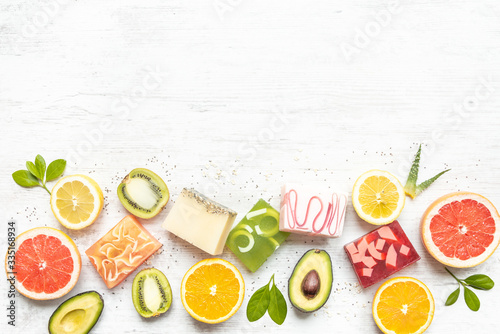 Top view of various colorful handmade organic soaps arranged with citrus fruits  herbs  chia seeds and aloe. White rusric background  copy space.