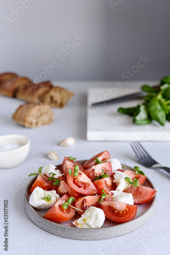 Italian Caprese salad with sliced tomatoes, mozzarella cheese, basil, olive oil in a plate on grey concrete table. Selective focus