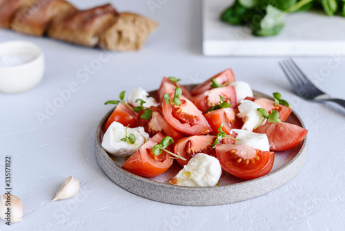 Italian Caprese salad with sliced tomatoes, mozzarella cheese, basil, olive oil in a plate on grey concrete table. Selective focus