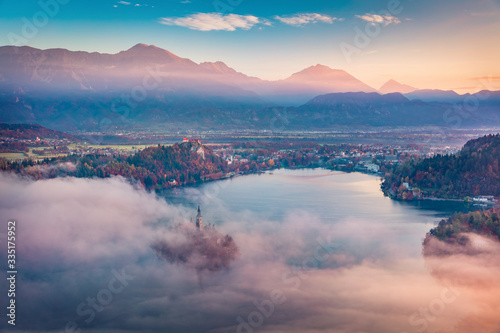 Fantastic sunrise on Bled lake. Misty morning view of church of Assumption of Maria on Bled lake. Foggy autumn landscape in Julian Alps, Slovenia, Europe. Traveling concept background..
