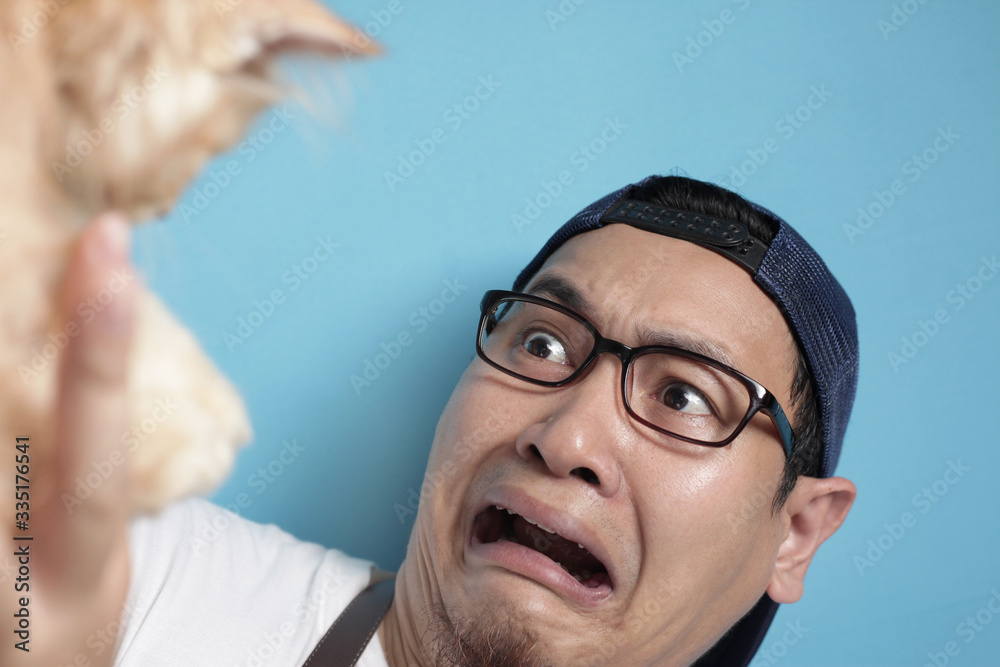 Fototapeta premium Man afraid of cat, funny face of a young Asian male scared or intimidated by kitten