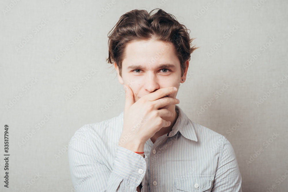 young man with hand over his mouth, stunned and speechless young man with hand over his mouth, stunned and speechless